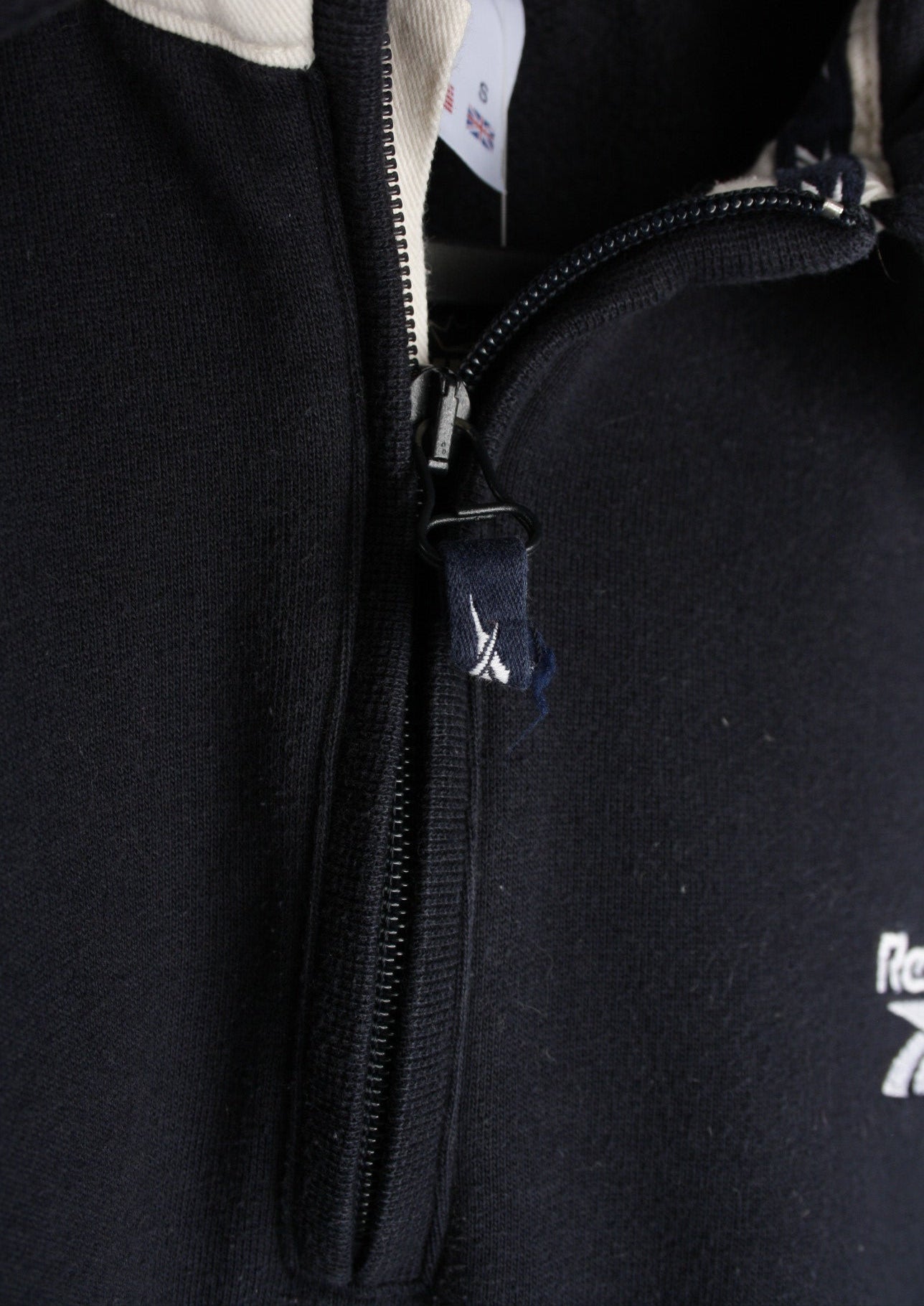 Close-up van de details van een marineblauwe Reebok quarter zip sweater in maat S, met hoogwaardige afwerkingen voor een sportieve uitstraling.
