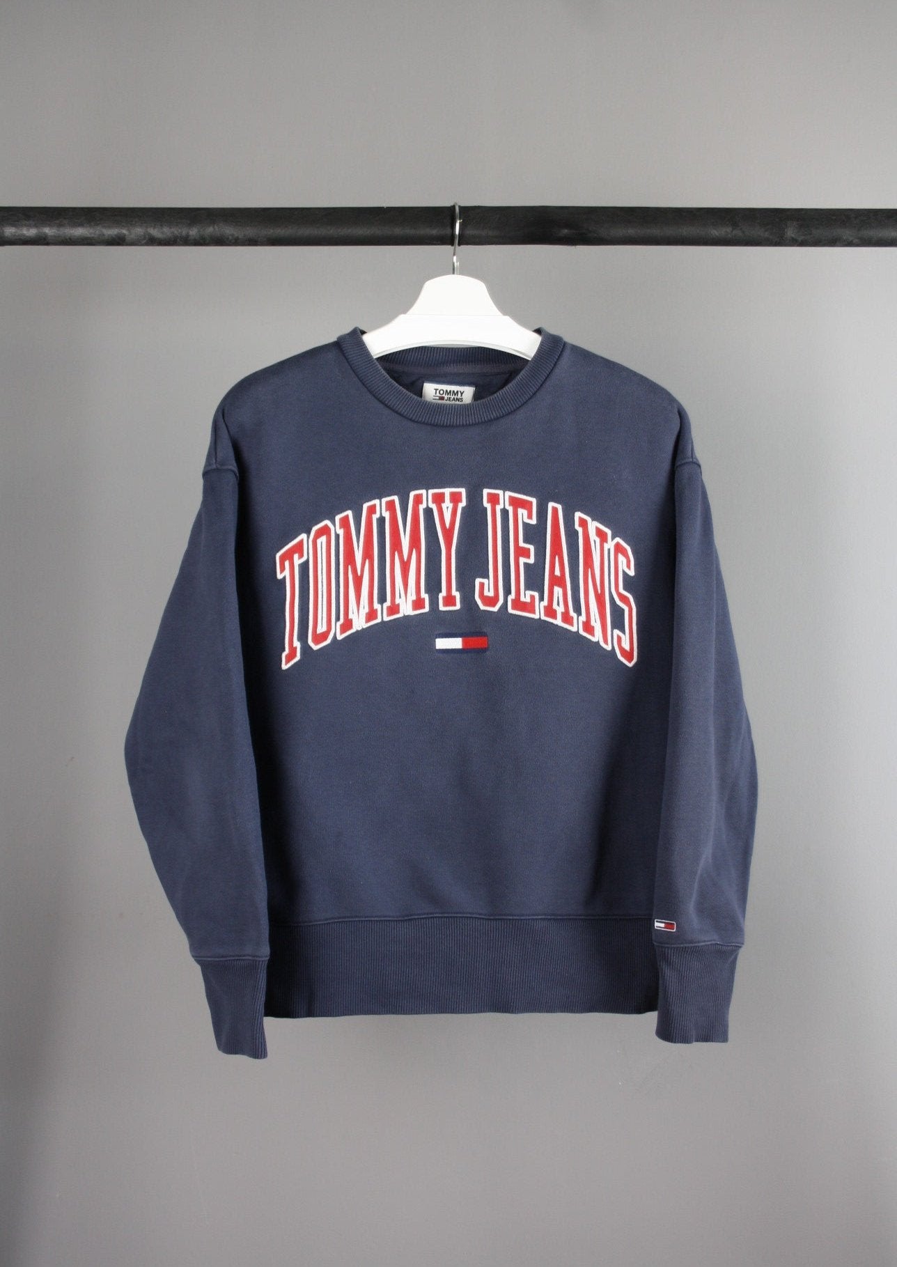 Voorkant van een marineblauwe Tommy Jeans sweater met grote rode tekst op de borst, gemaakt van een comfortabele en zachte stof.