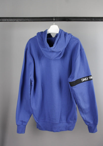 Achterkant van een blauwe Daily Paper Captain hoodie met een zwarte band op de rechterarm, ideaal voor een moderne en stijlvolle look.