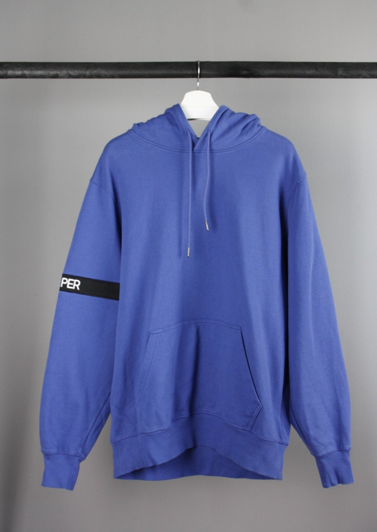 Voorkant van een blauwe Daily Paper Captain hoodie met een zwarte band om de rechterarm, gemaakt van een zachte en comfortabele stof voor een casual uitstraling.