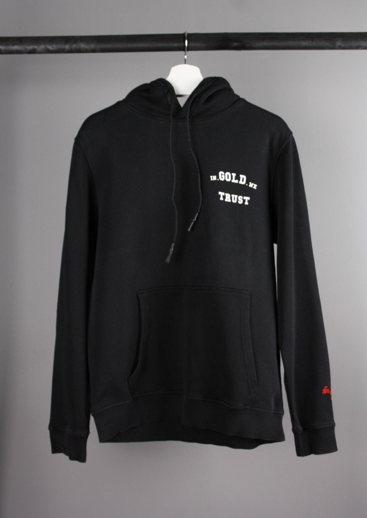 Voorkant van een zwarte 'In Gold We Trust' hoodie met het merklogo op de borst en een capuchon, gemaakt van een zachte en comfortabele stof.