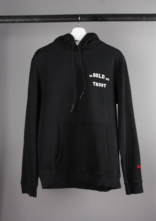 Voorkant van een zwarte 'In Gold We Trust' hoodie met het merklogo op de borst en een capuchon, gemaakt van een zachte en comfortabele stof.