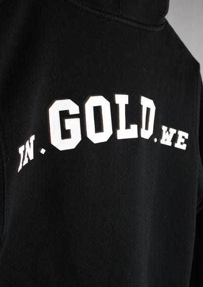 Close-up van het grote witte In Gold We Trust logo op de achterkant van een zwarte hoodie, met strakke print en premium afwerking voor een moderne streetwear uitstraling."