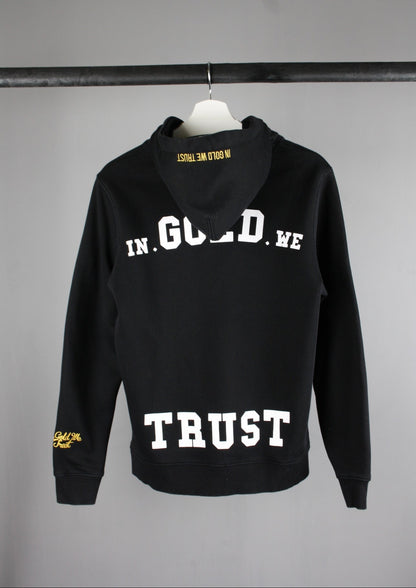 Achterkant van een zwarte In Gold We Trust hoodie met groot wit logo, ideaal voor een trendy en urban look.