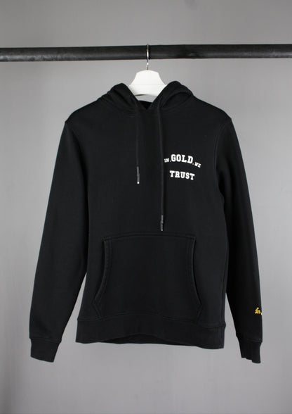 Voorkant van een zwarte In Gold We Trust hoodie met een wit logo op de borst, casual en streetwear geïnspireerd design.