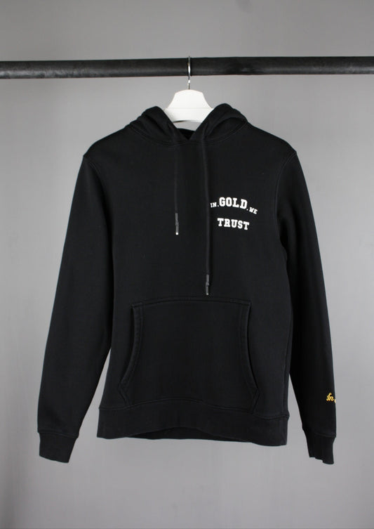 Voorkant van een zwarte In Gold We Trust hoodie met een wit logo op de borst, casual en streetwear geïnspireerd design.