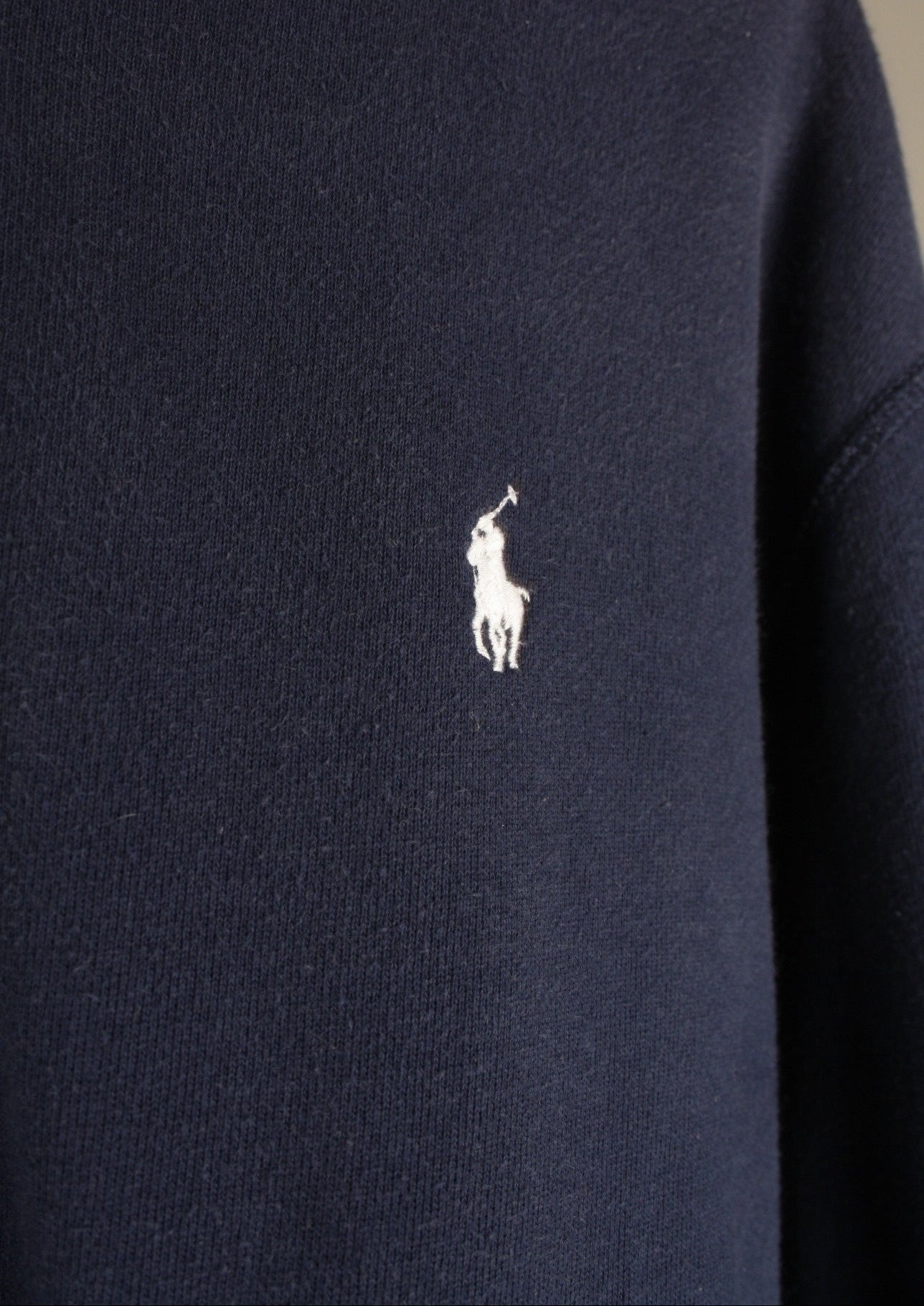 Close-up van het wit geborduurde paardje op de voorkant van een marineblauw Ralph Lauren vest, het herkenbare logo van het merk.