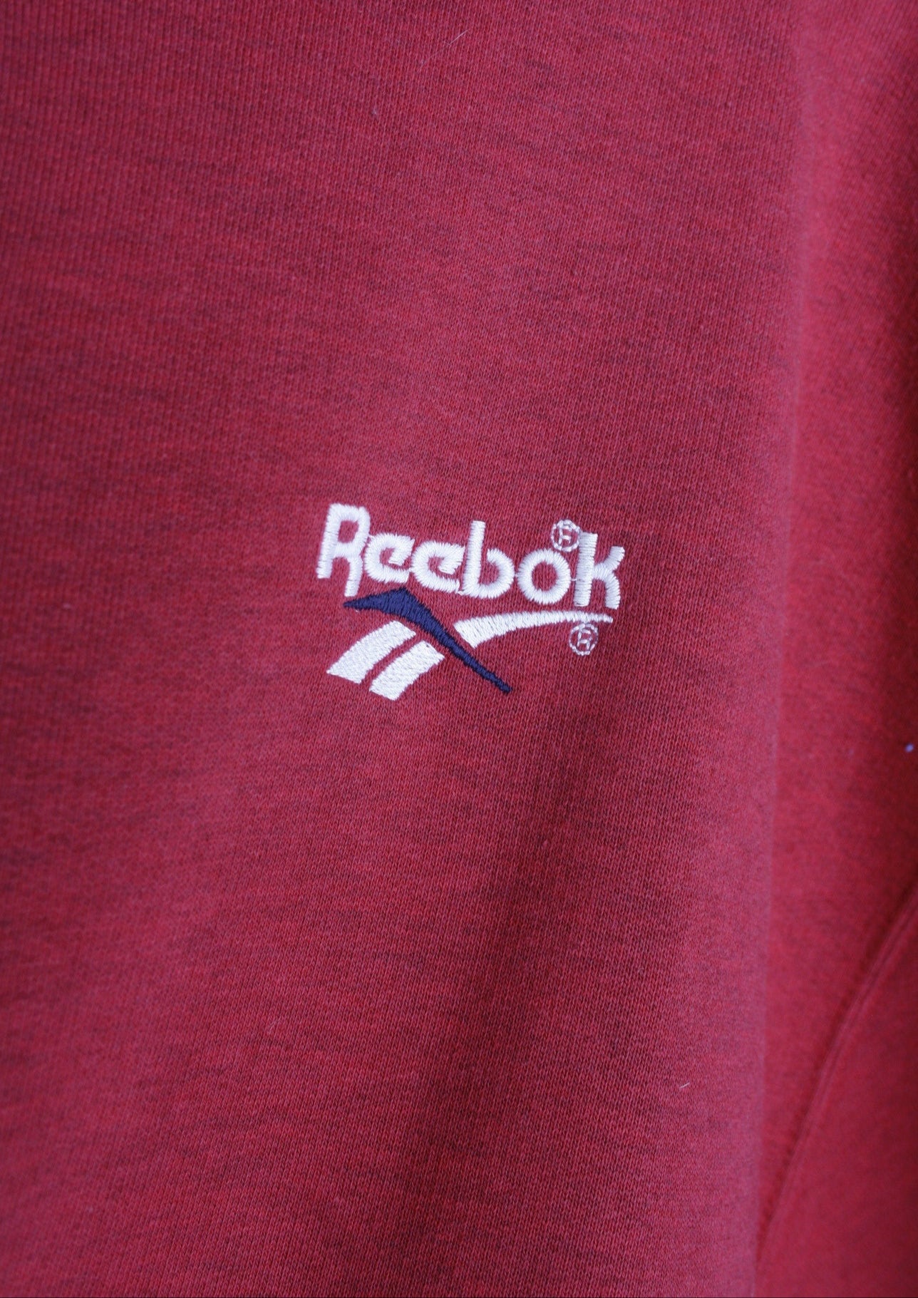 Close-up van het wit geborduurde logo links op de borst van een rode Reebok sweater.