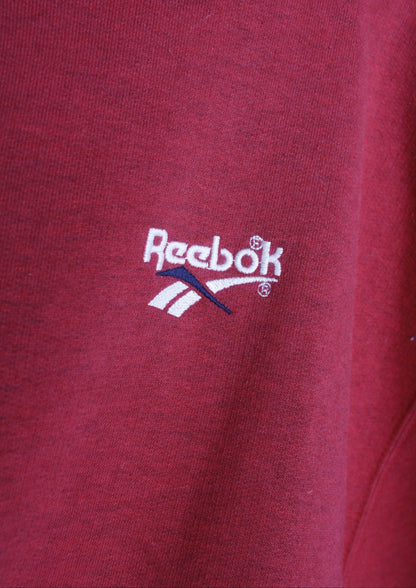 Close-up van het wit geborduurde logo links op de borst van een rode Reebok sweater.