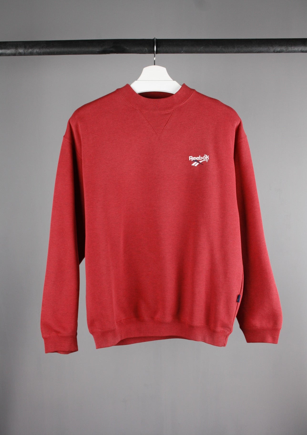 Voorkant van een rode Reebok sweater met een wit geborduurd logo links op de borst, voor een sportieve en casual uitstraling.