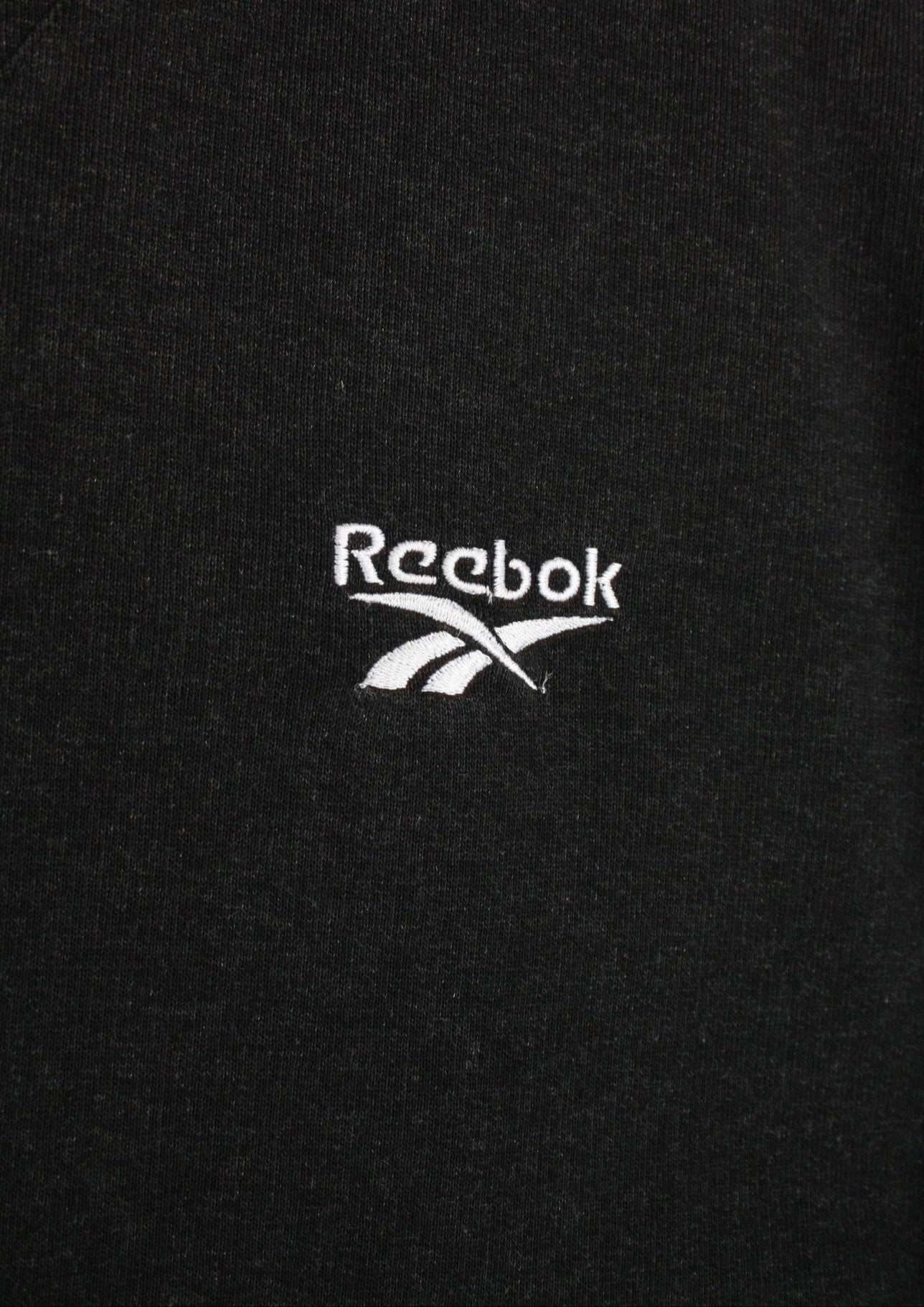 Close-up van het wit geborduurde logo linksboven op de voorkant van een zwarte Reebok sweater in maat L
