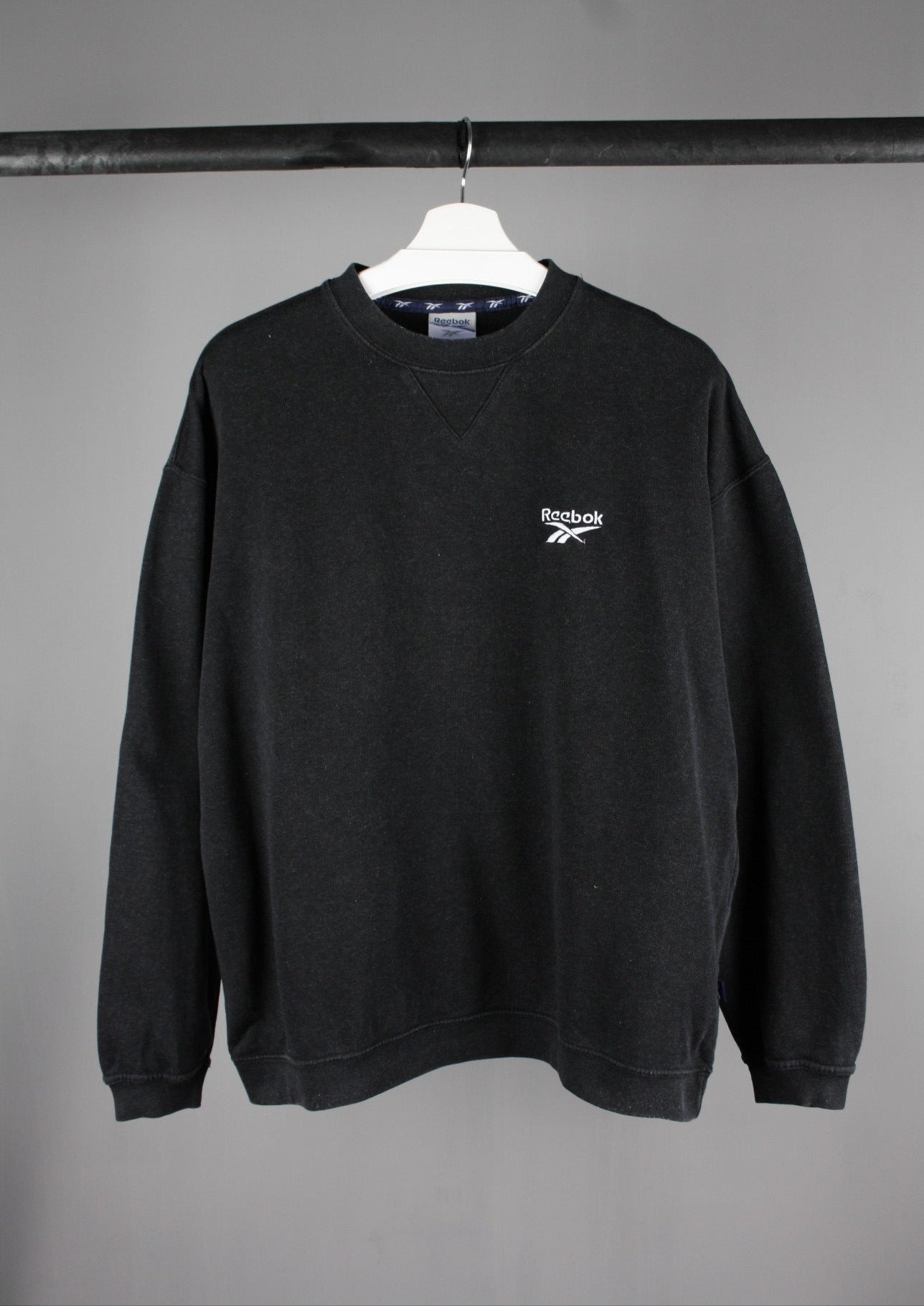 Voorkant van een zwarte Reebok sweater in maat L met een wit geborduurd logo linksboven, voor een sportieve en casual uitstraling.