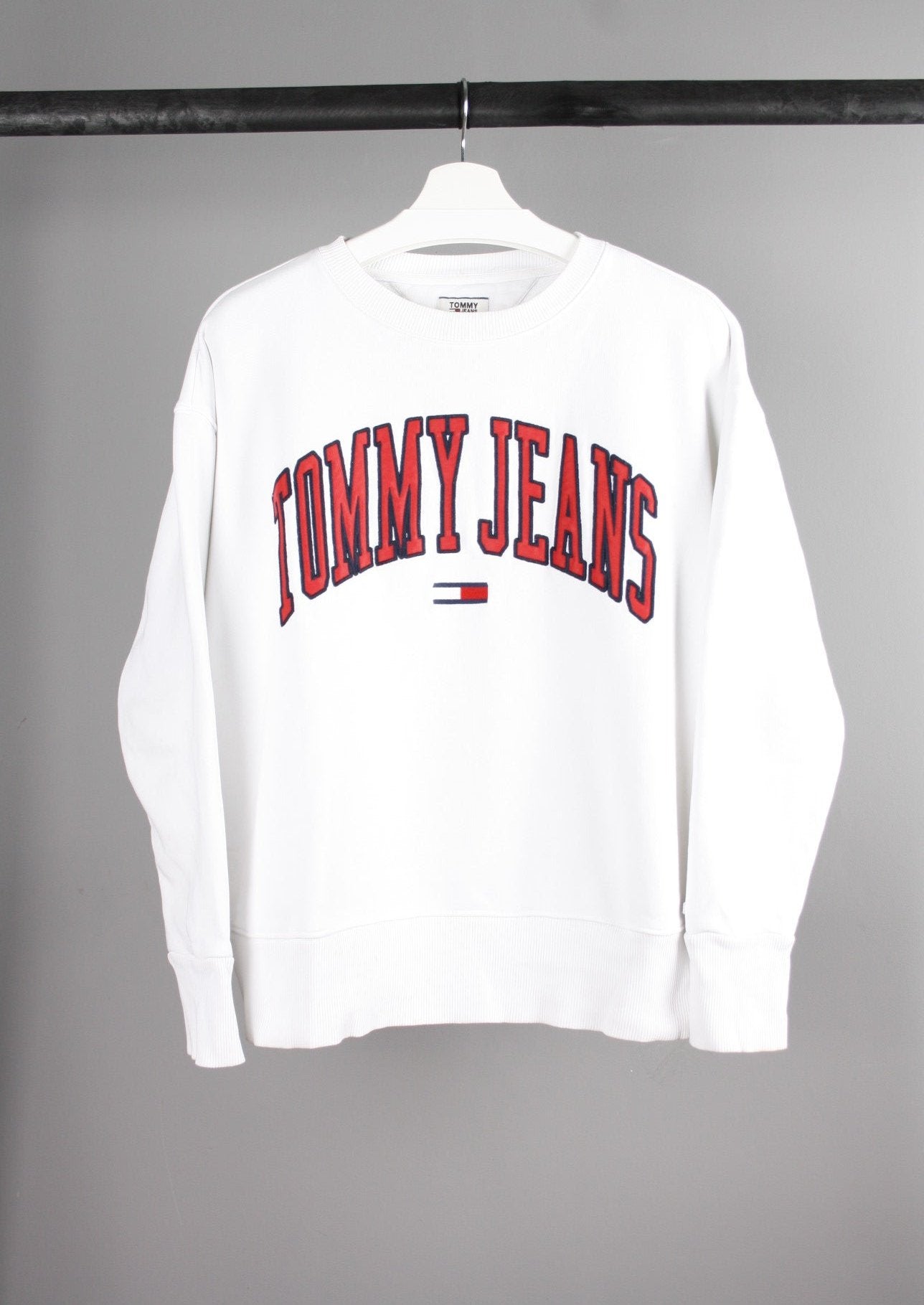 Voorkant van een witte Tommy Jeans sweater met grote rode tekst op de borst, gemaakt van zachte, comfortabele stof.